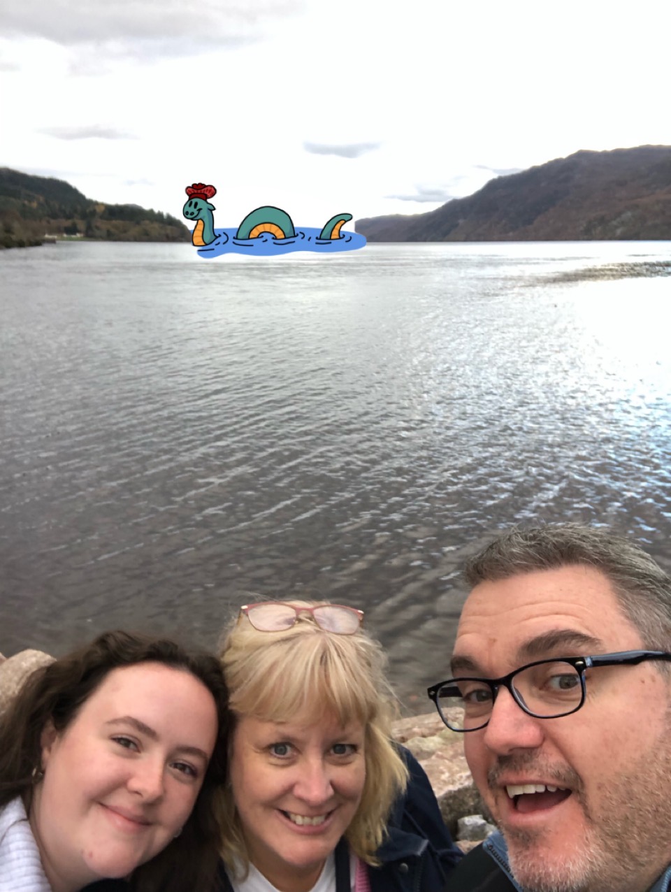 three people in front of a lake with a cartoon montser in the back